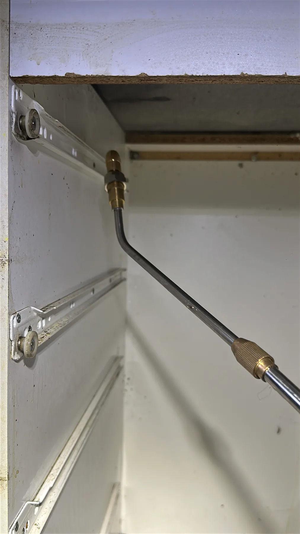 Metal pest-control application wand positioned inside an emptied kitchen cabinet