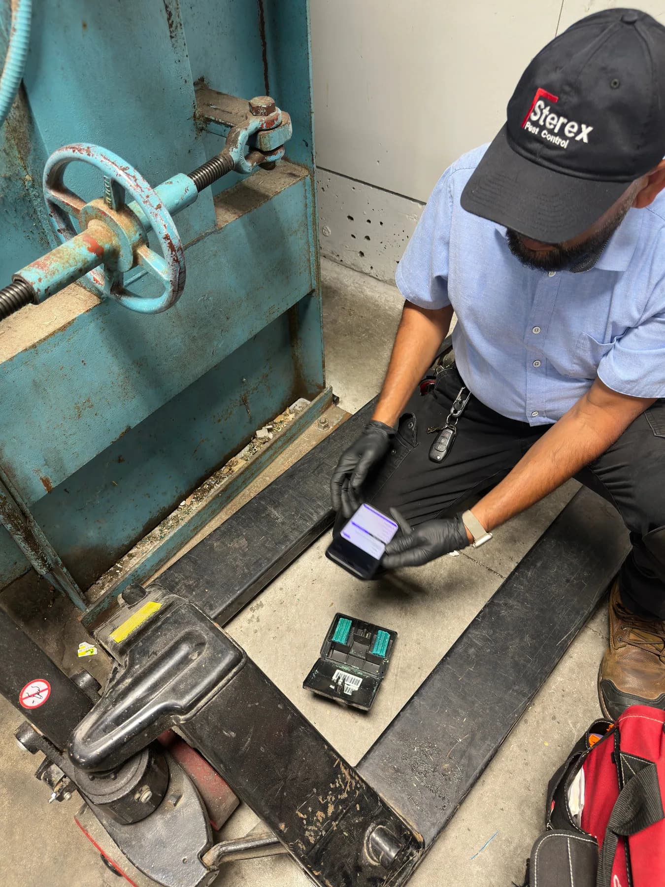 Sterex technician logging a serviced rodent bait station on a phone beside the waste compactor of a North York commercial building