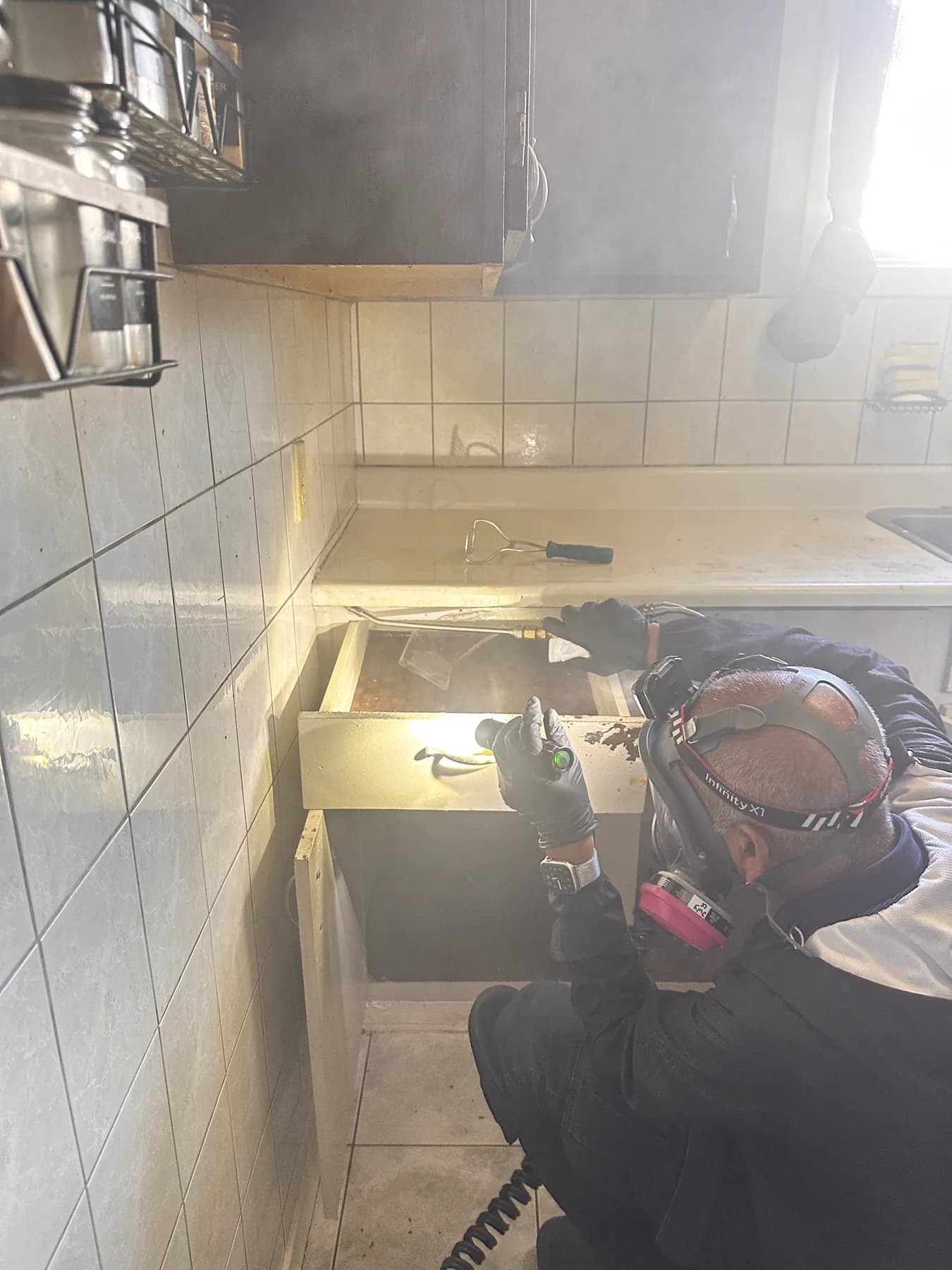 Technician using an application wand inside an open kitchen cabinet