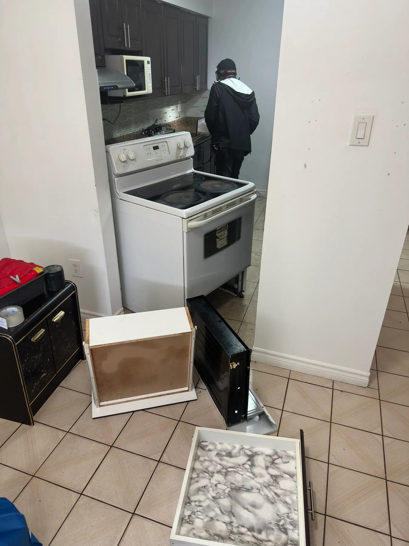 Pest control technician inspecting a kitchen with appliances and drawers pulled out