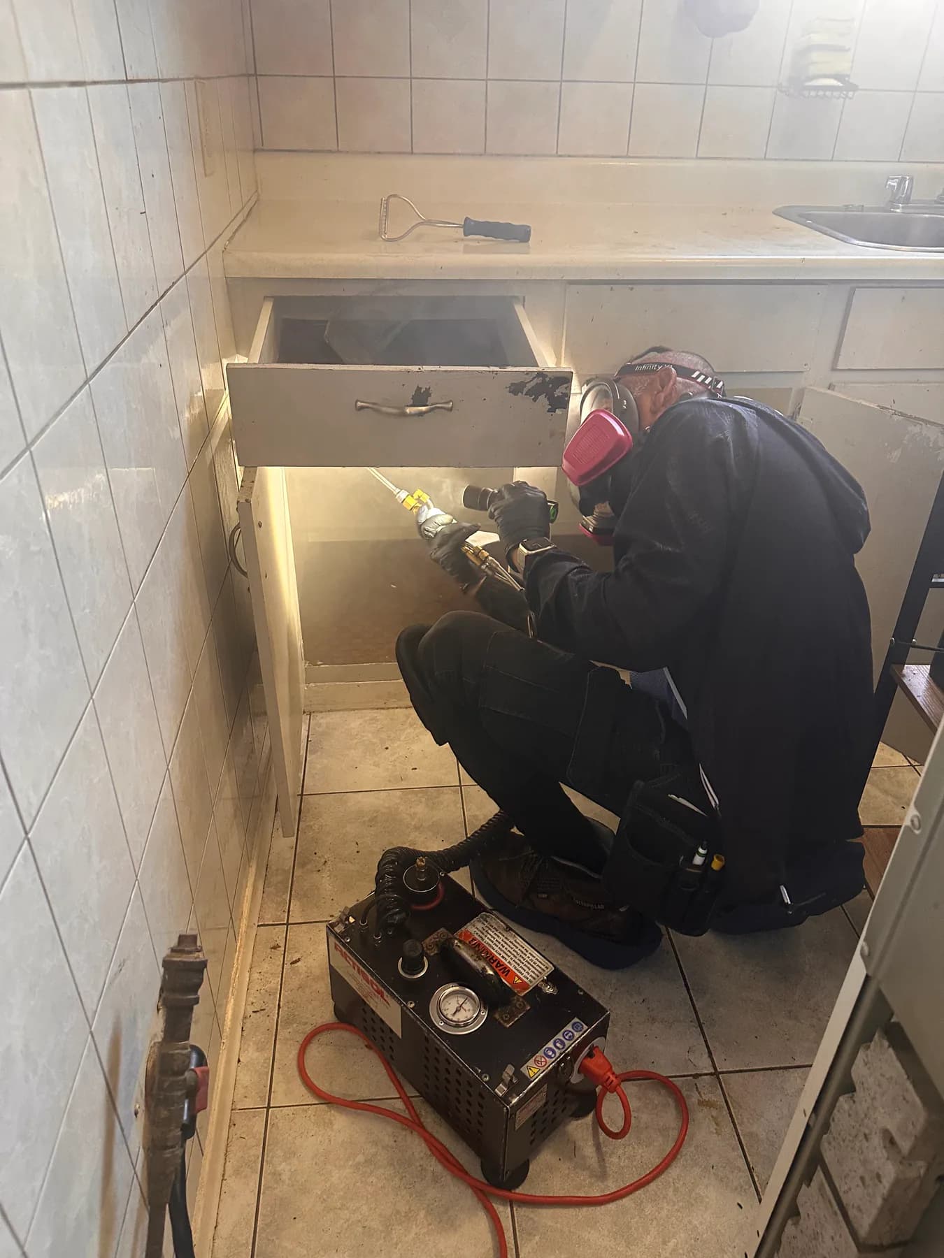 Pest control technician applying treatment inside an open kitchen cabinet