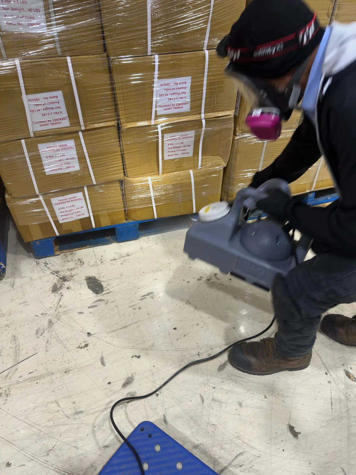 Sterex technician in a respirator and face shield fogging beside palletized spice product in a warehouse