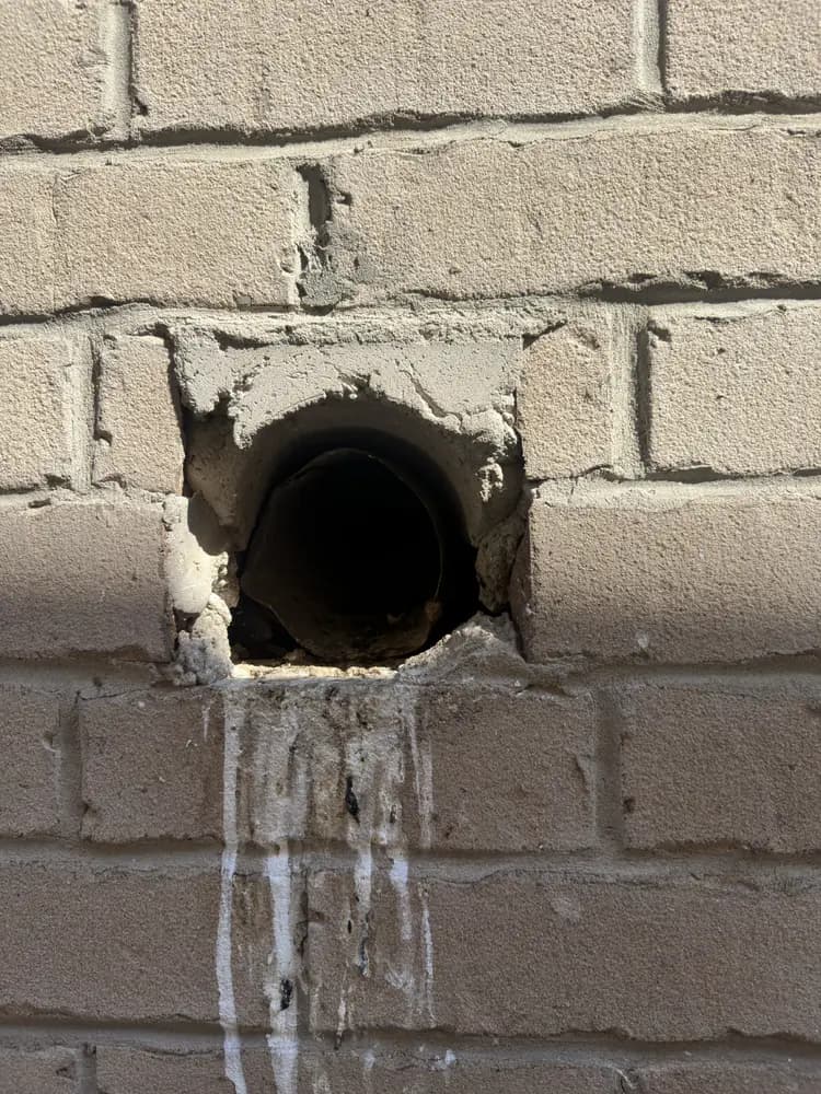 Round unsealed vent opening cut through an exterior brick wall