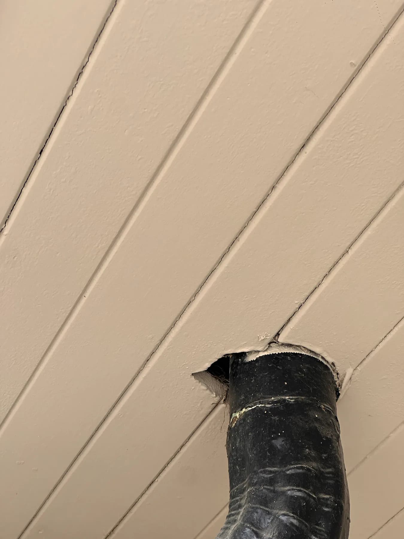 Black vent pipe passing through a ceiling opening without a visible perimeter seal